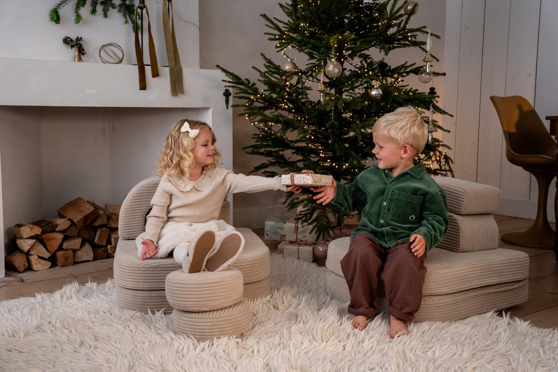 Twee kinderen geven elkaar een cadeau bij de kerstboom
